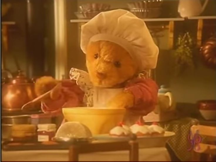 a teddy bear dressed as a chef mixing food in a bowl with a spoon on the table