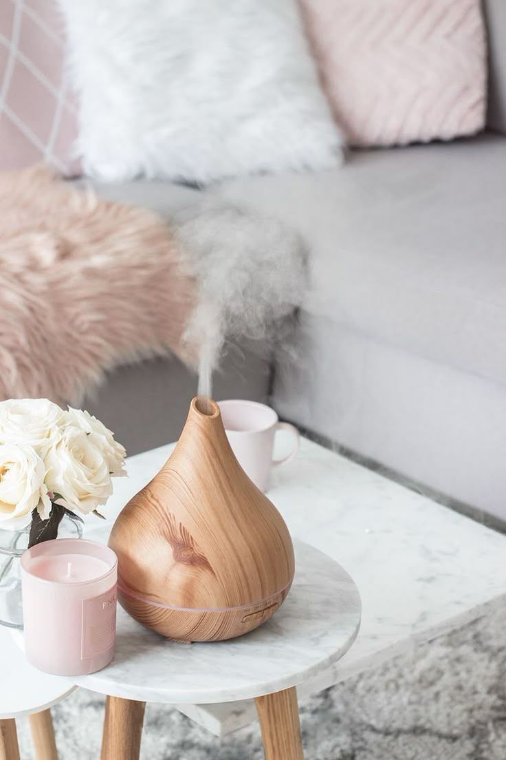 a white table topped with a vase filled with flowers next to a gray couch and pink pillows