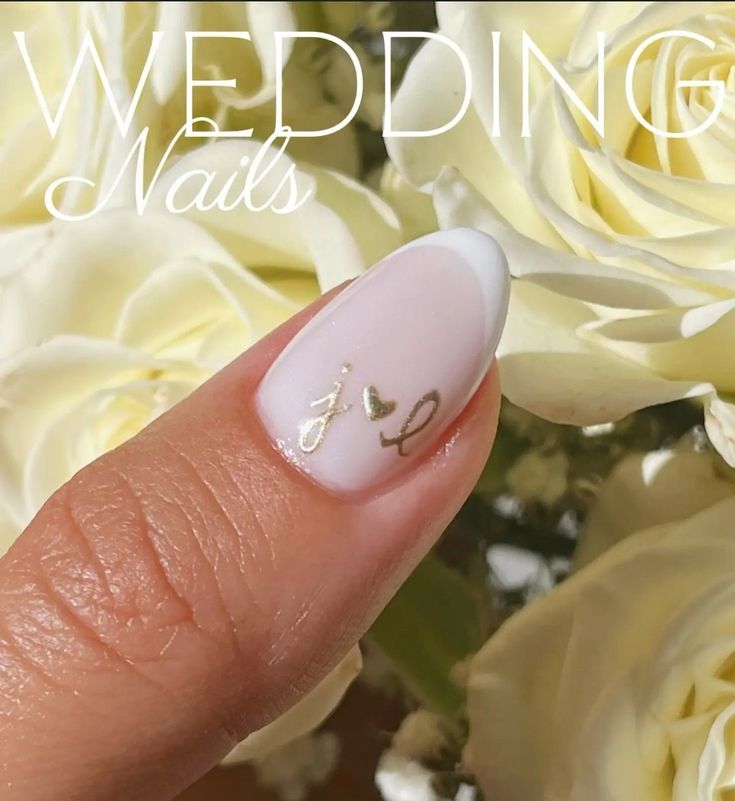 a woman's hand with white and gold nail polish on it, next to flowers