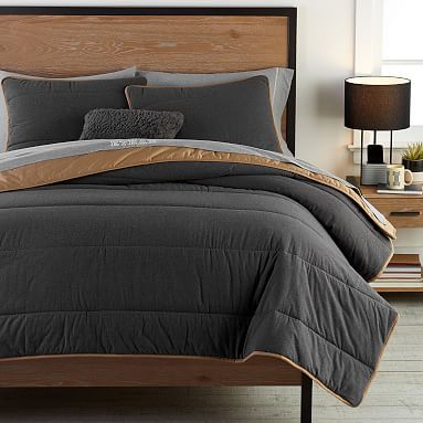 a bed with grey and brown comforter in a bedroom next to a lamp on a table