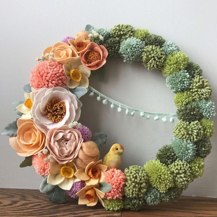 a wreath made out of fake flowers on top of a wooden table next to a wall