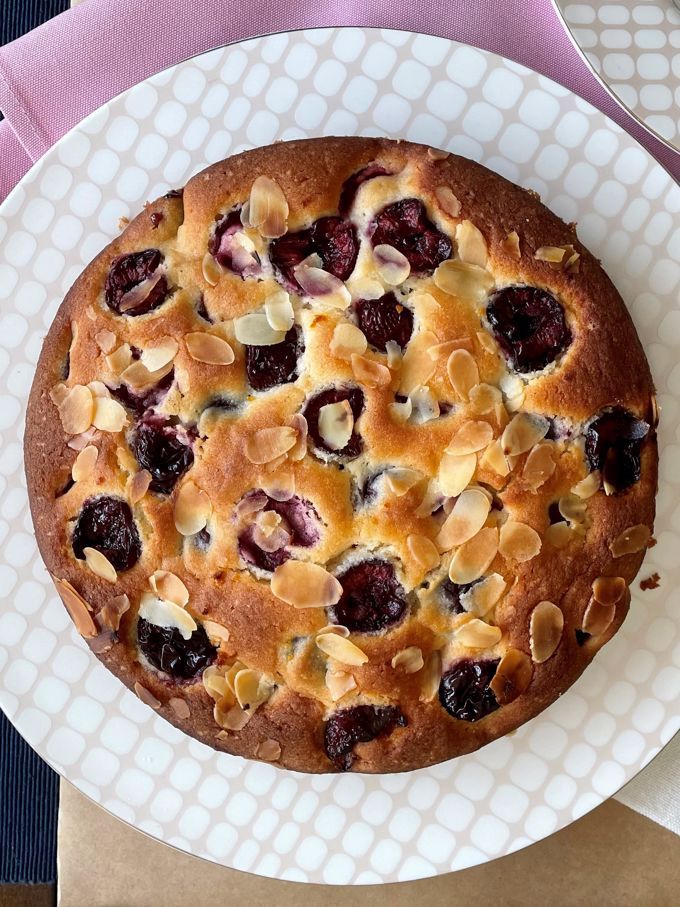 a white plate topped with a cake covered in nuts and cherries on top of a table