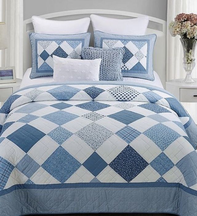 a blue and white quilted bed in a bedroom with flowers on the nightstands