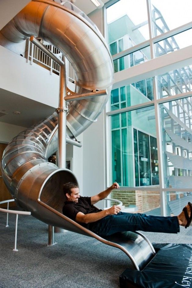 a man sitting on top of a slide next to a large glass window in a building