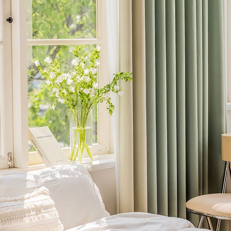 a vase with flowers in it sitting on a window sill next to a bed