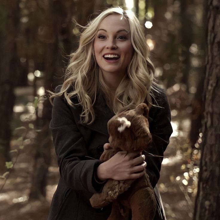 a woman holding a teddy bear in the woods