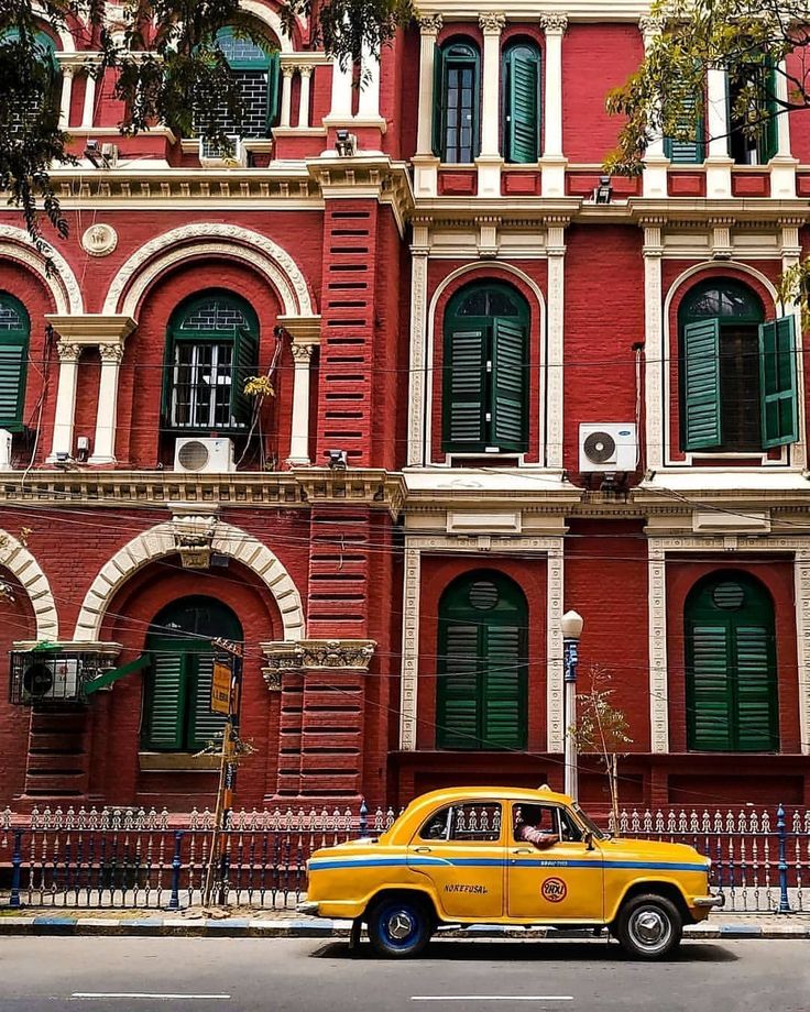 a yellow taxi cab is parked in front of an old red building with green shutters