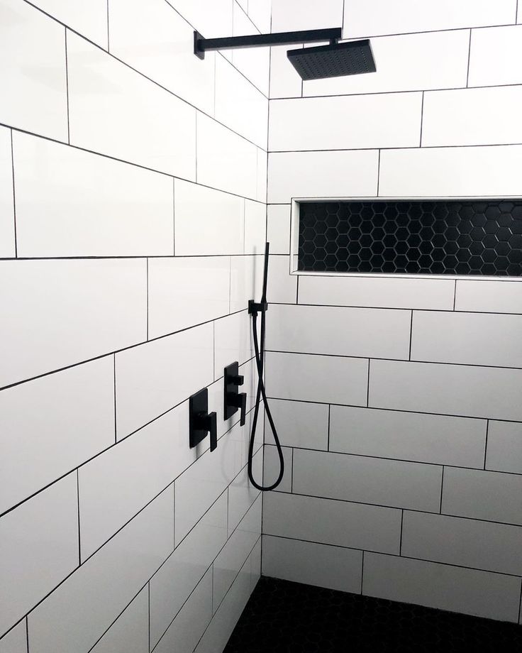 a white tiled shower with black grouting on the wall and floor, next to a walk in shower head