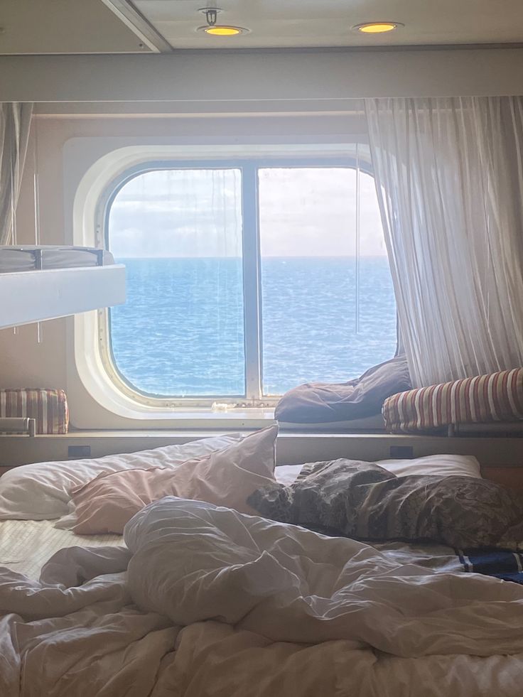 there is a bed with white sheets and pillows next to a window on the ship