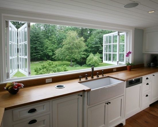 a kitchen with white cabinets and wooden counter tops next to a large window that looks out onto the yard