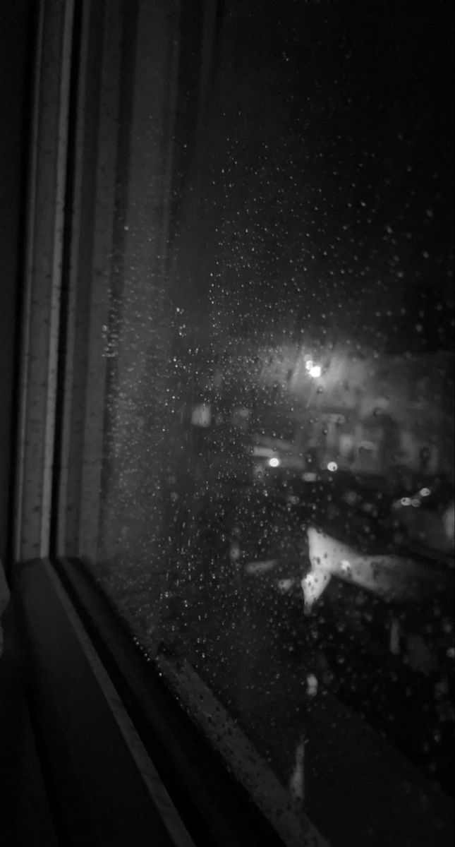 black and white photograph of rain coming down on the window sill at night time