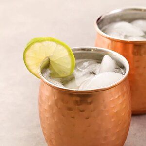 two copper mugs filled with ice and lime wedged into the rim, one holding a lime