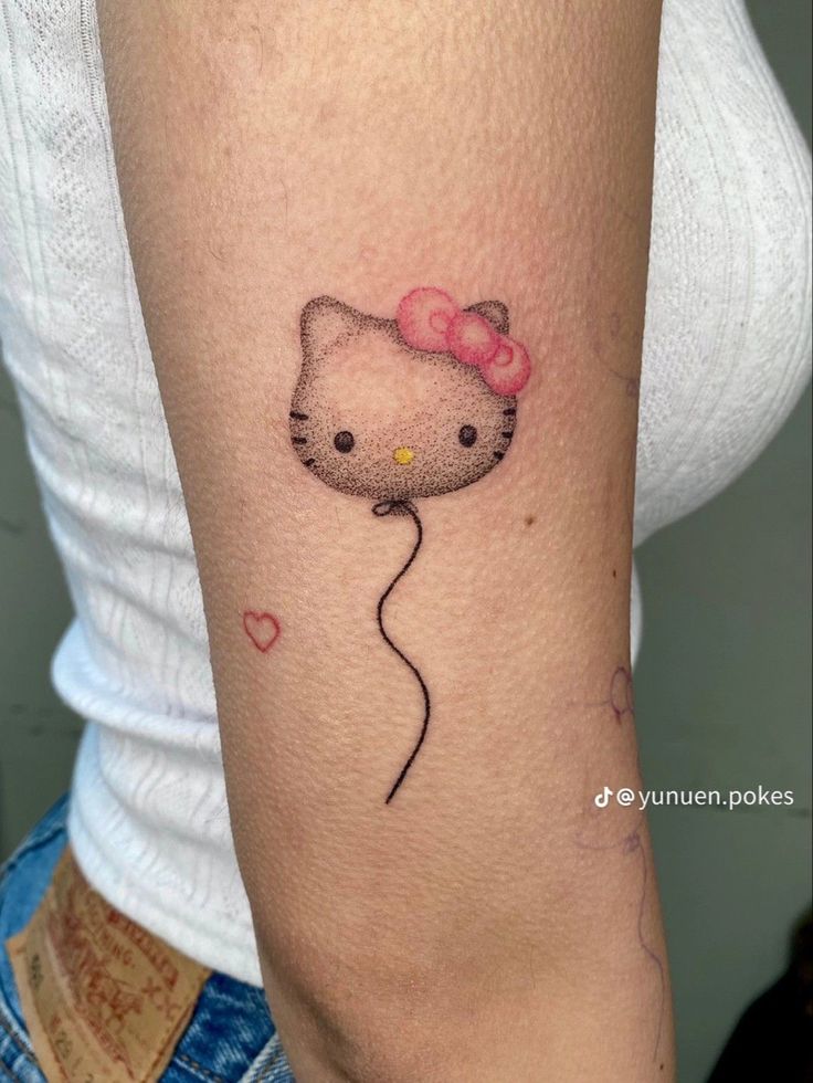 a hello kitty tattoo on the arm with a pink bow and balloon attached to it