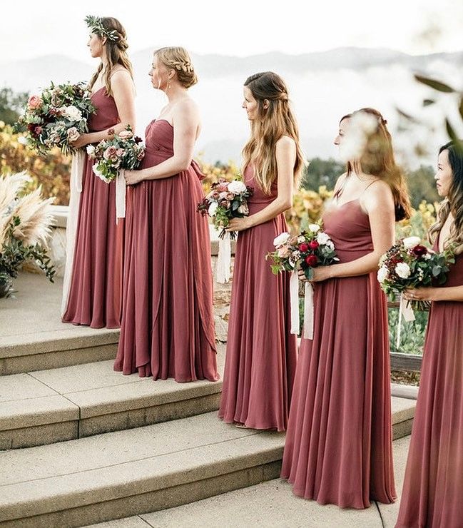 bridesmaids in red dresses standing on steps with their bouquets and looking at each other