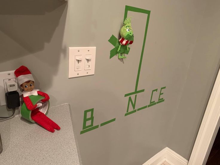 an elf is sitting on the counter next to a wall with green letters that spell out his name