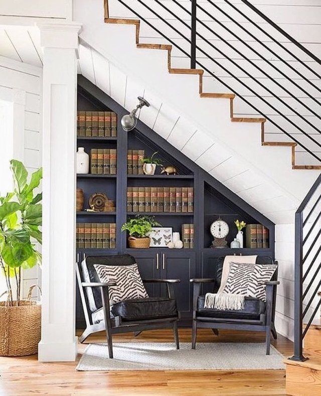 a living room filled with furniture and bookshelves next to a stair case full of books