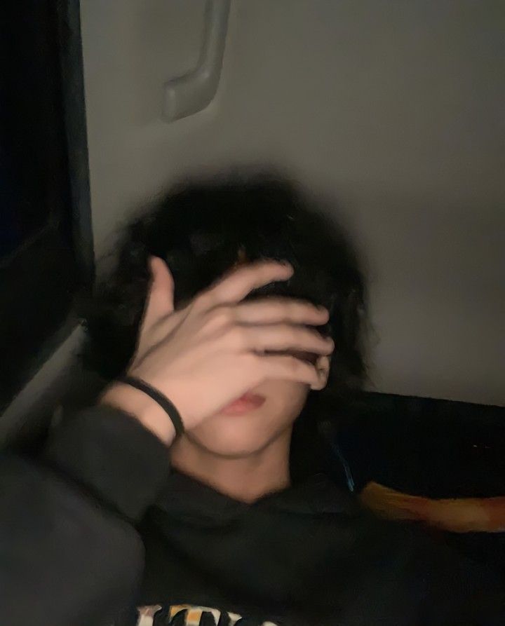 a man covering his face with his hands while sitting on a bus in the dark