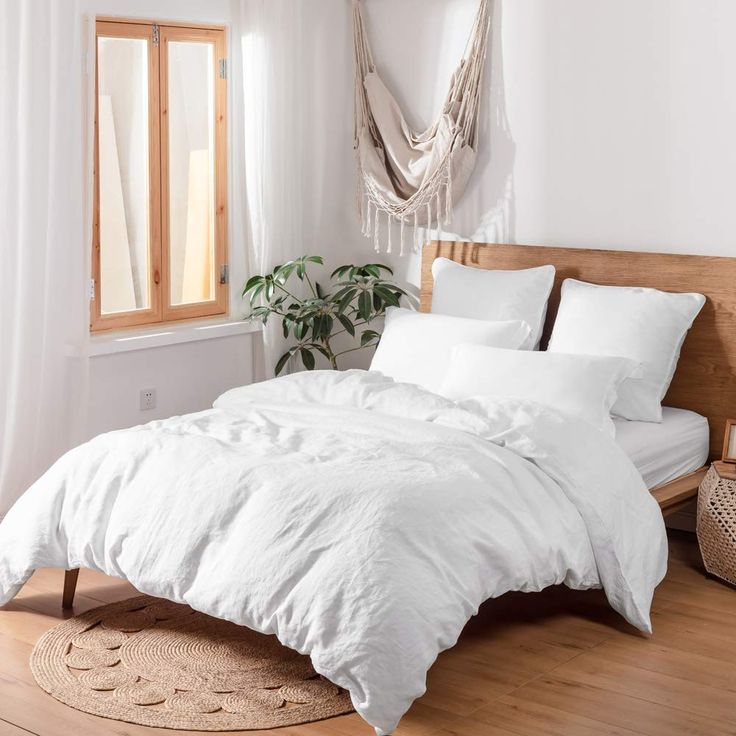 a bed with white linens and pillows in a room next to a potted plant