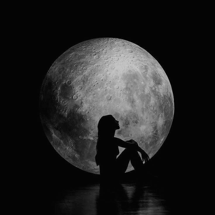 a black and white photo of a woman sitting in front of the moon