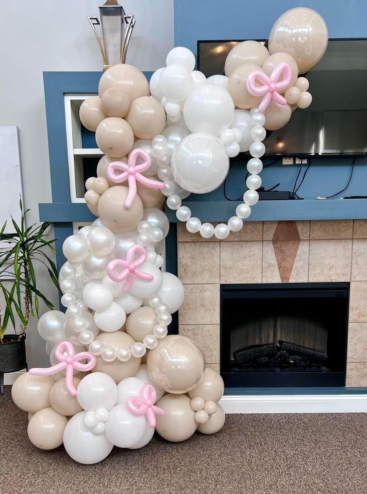 a bunch of balloons that are in front of a fireplace with pink bows on them