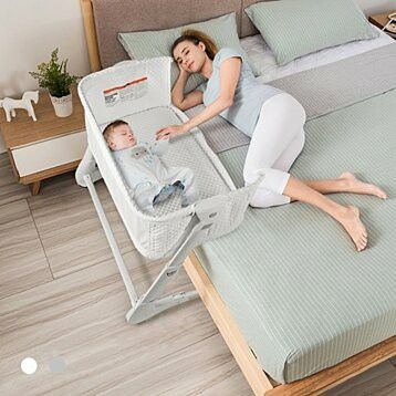 a woman laying on top of a bed next to a baby in a crib