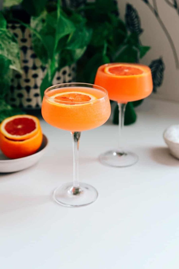 two wine glasses filled with orange juice and garnished with grapefruit