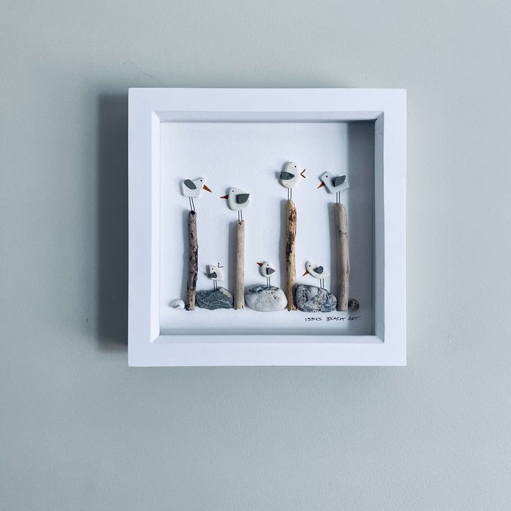 three birds are sitting on sticks in a shadow box with rocks and sand behind them