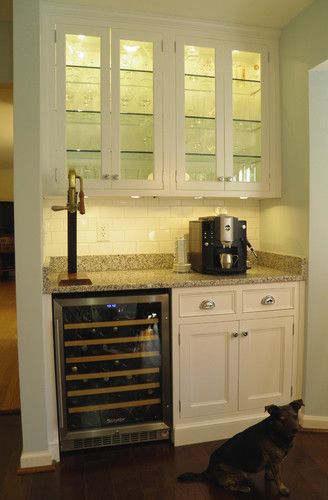 a wine cooler in the corner of a kitchen with white cabinets and marble counter tops