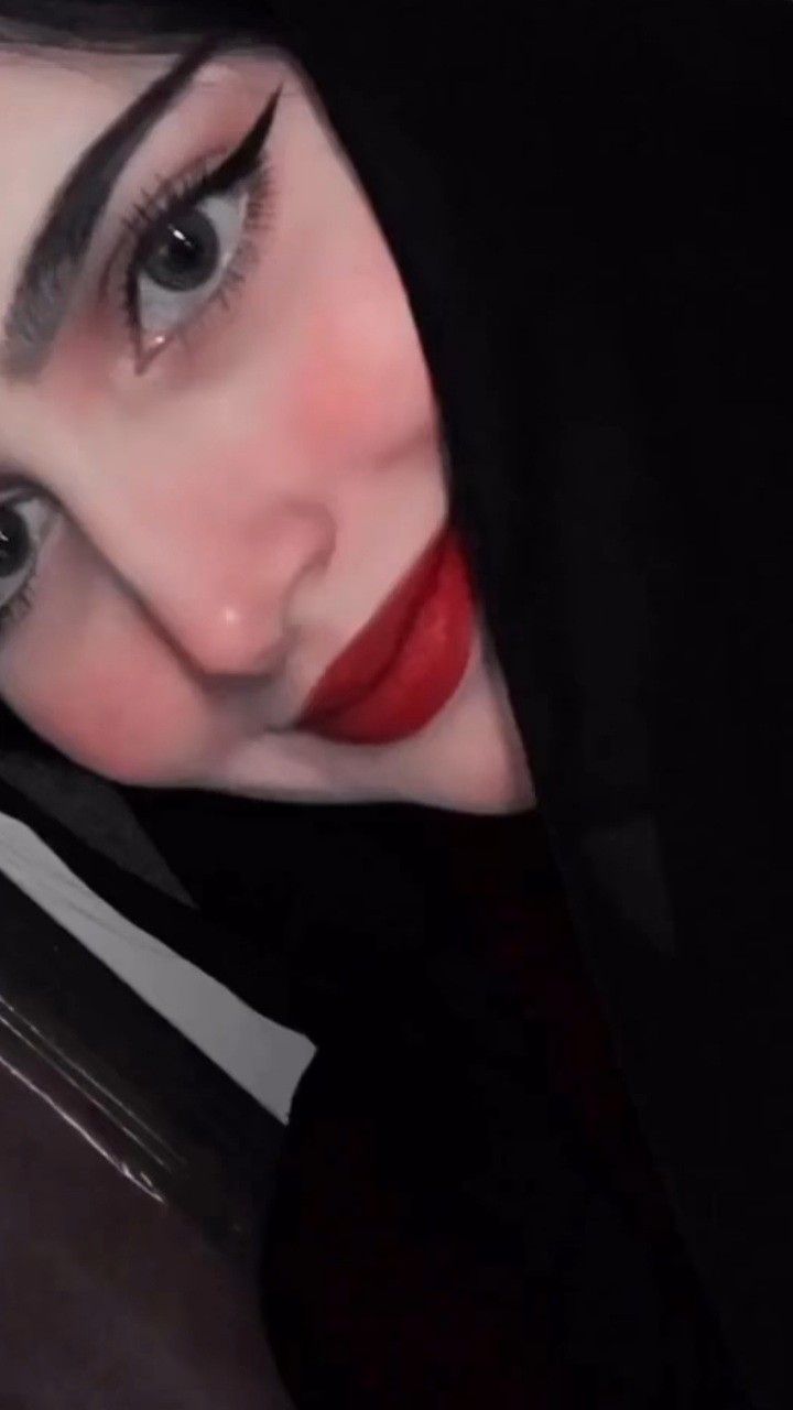 a woman with black hair and red lipstick wearing a hoodie looking at the camera