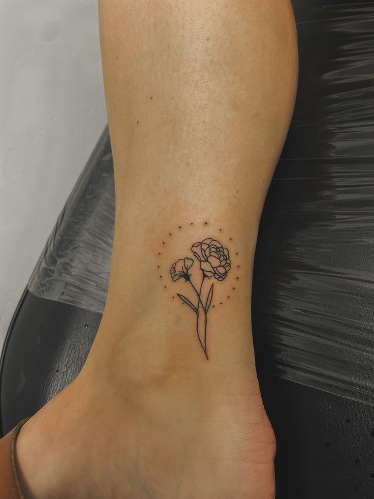 a small flower tattoo on the side of a woman's foot with dots around it