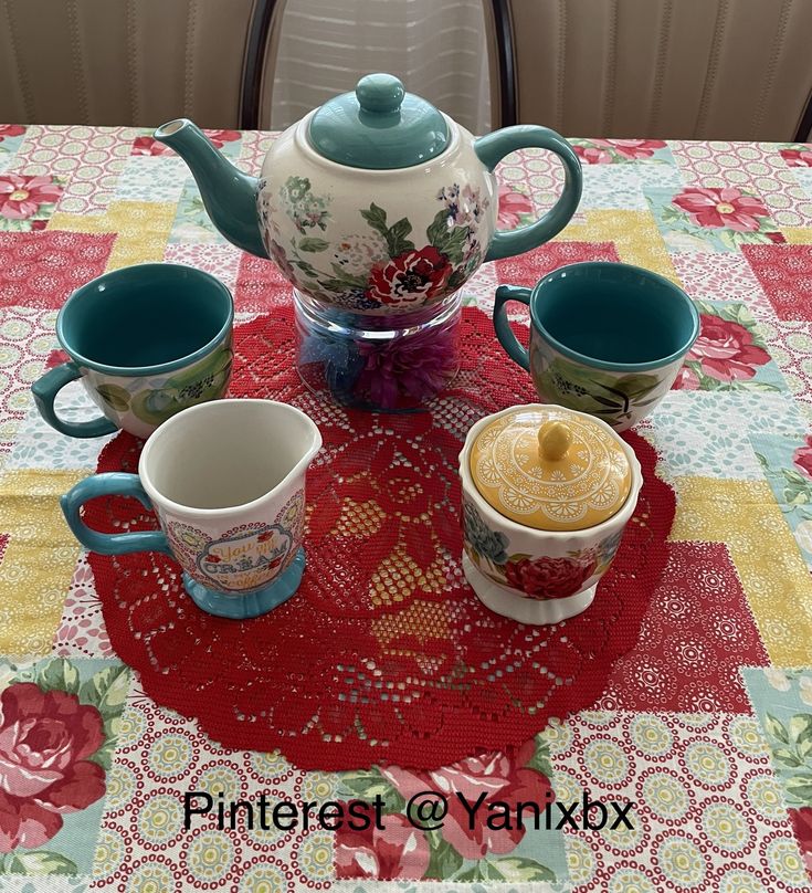 a table topped with cups and a teapot on top of a red doily