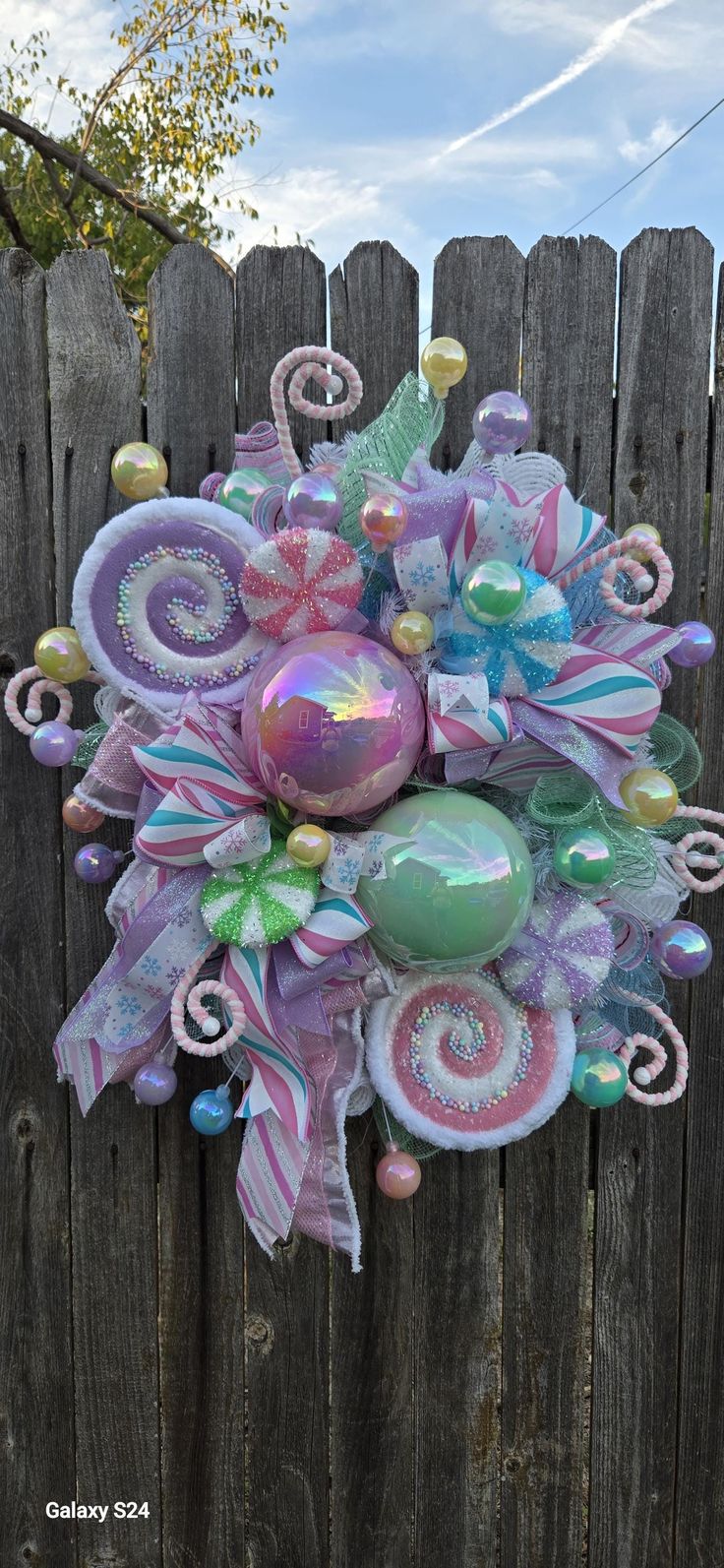 a wreath made out of balloons and ribbons on a wooden fence with blue sky in the background