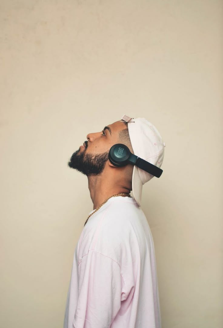 a man with headphones on his ears looking up to the sky in front of a beige wall