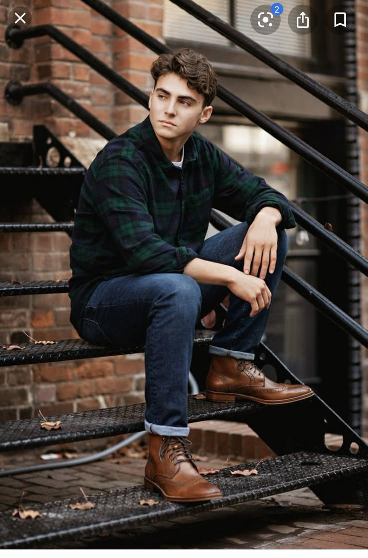 a young man sitting on the steps in front of a brick building wearing brown shoes