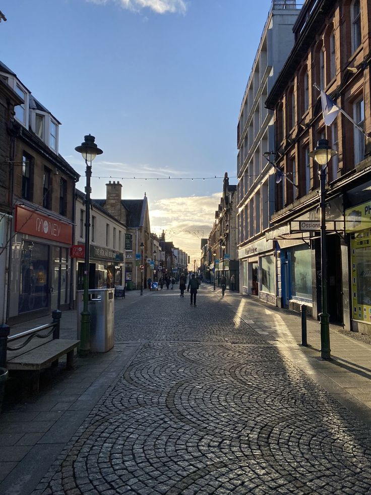 a cobblestone street lined with buildings and people walking on the sidewalk in front of them