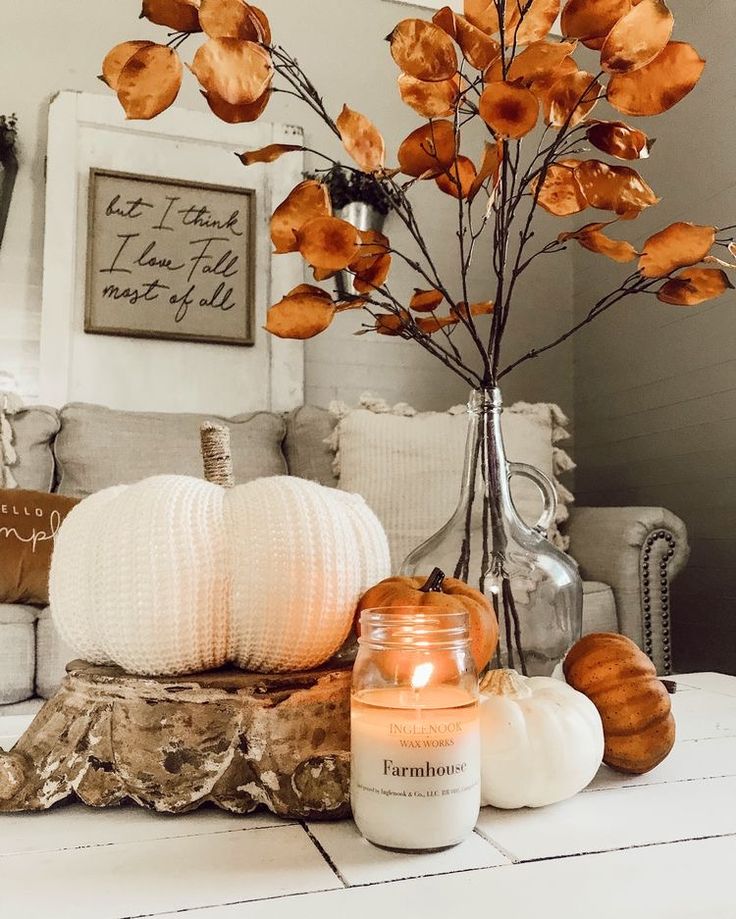 pumpkins and candles on a table in front of a white couch with an orange flower