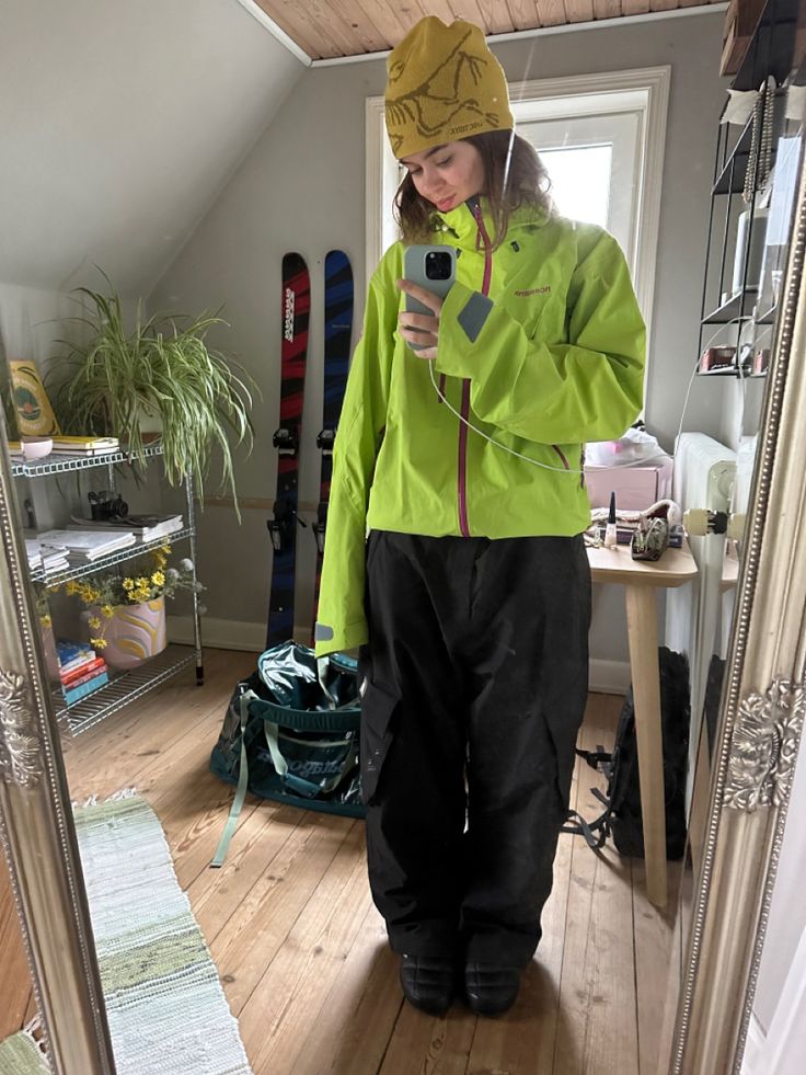 a woman standing in front of a mirror looking at her cell phone while wearing skis