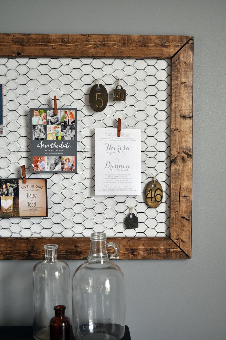 a wooden frame with magnets and pictures on the wall next to two glass bottles