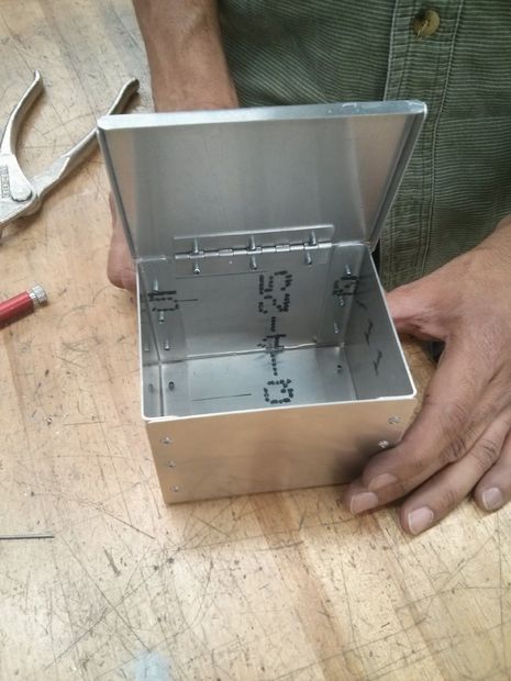 a man is holding an open box on a wooden table next to tools and other items