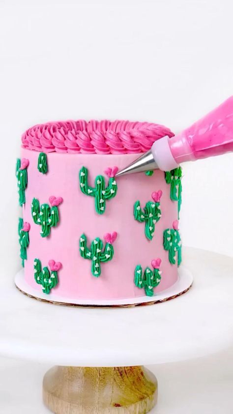 a cake decorated with pink icing and green cacti is being frosted