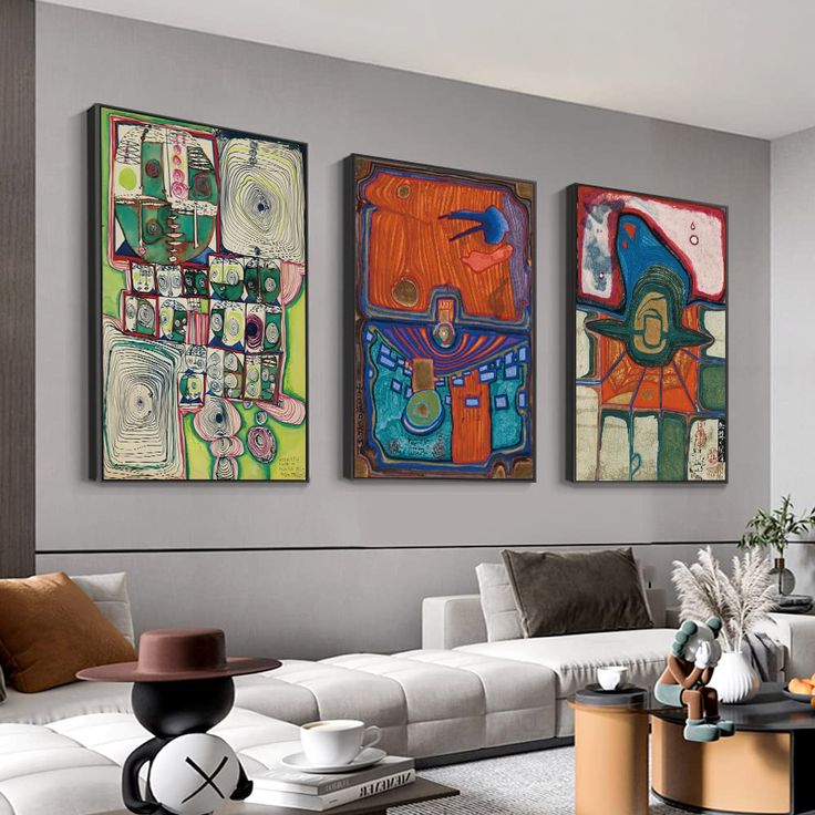 three paintings hang on the wall above a white couch in a living room with modern furniture