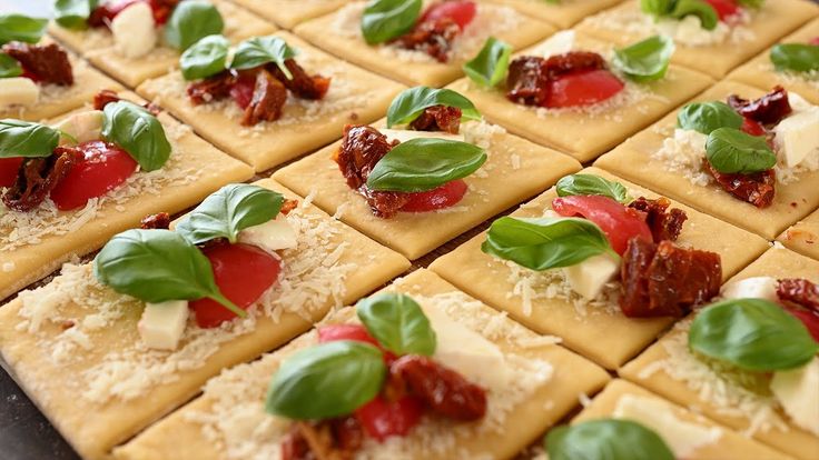 small crackers with cheese, tomatoes and basil on them are ready to be eaten