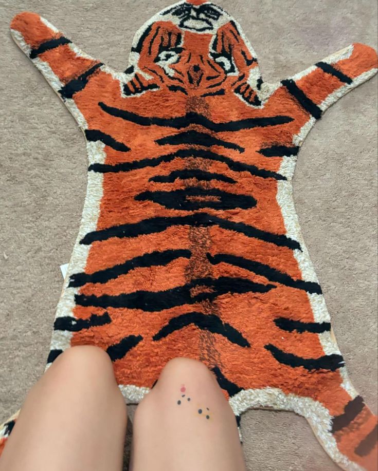 someone is laying down on the floor with their legs crossed and there is a rug that looks like a tiger