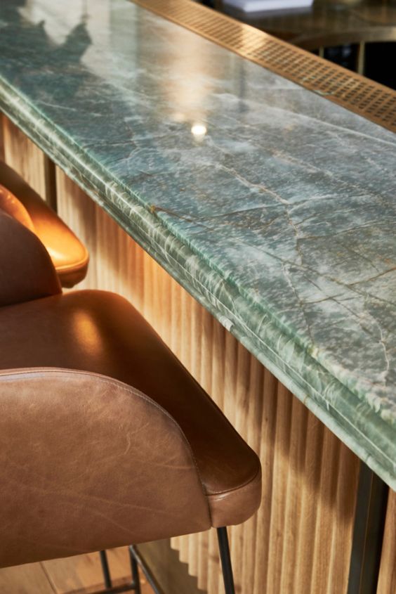 two brown leather chairs sitting next to a green marble counter top with barstools