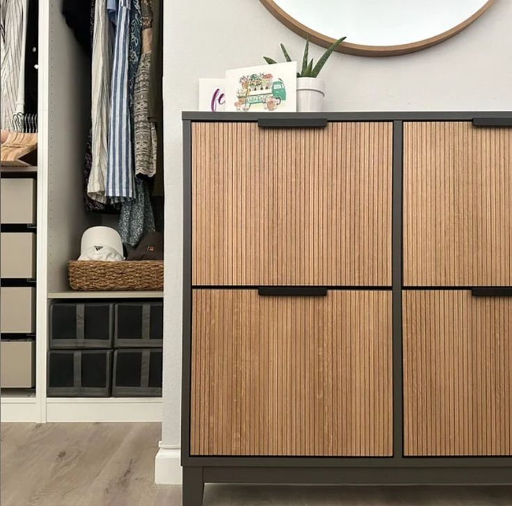 a wooden cabinet sitting in the corner of a room with clothes hanging on shelves and a mirror above it