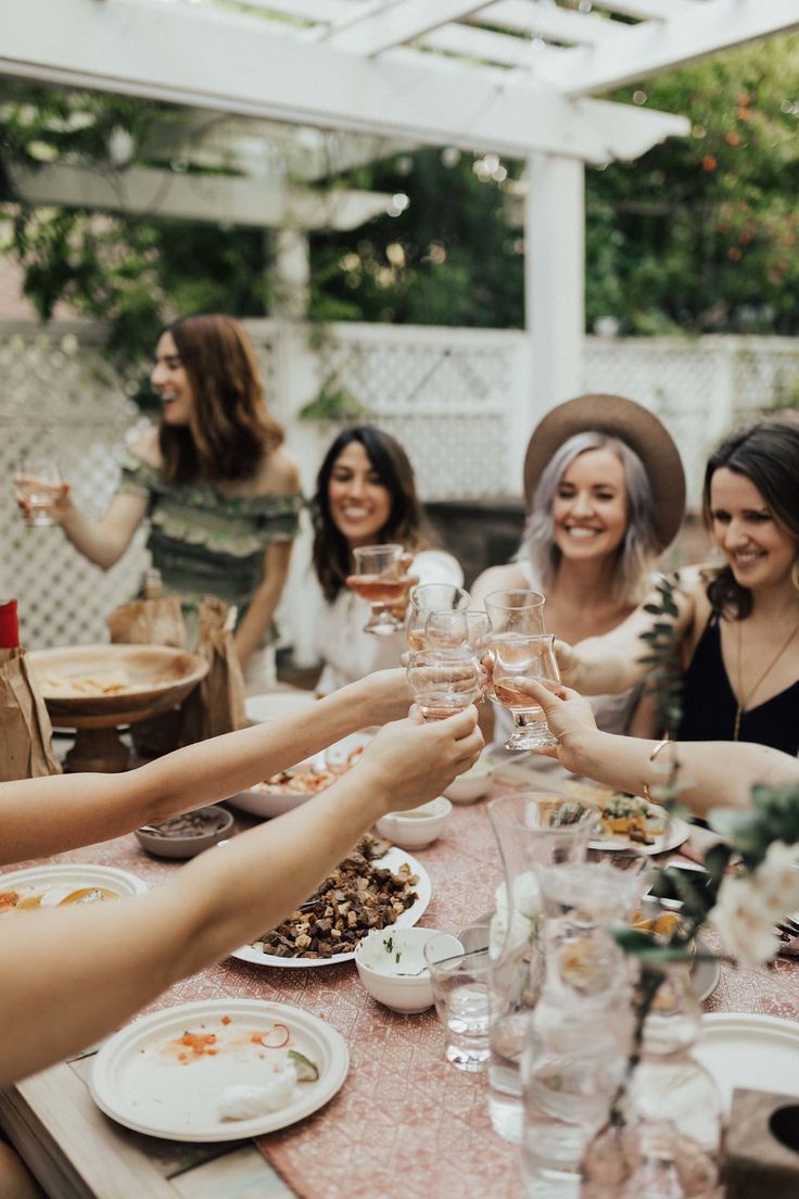 a group of women sitting around a table toasting with wine glasses in their hands