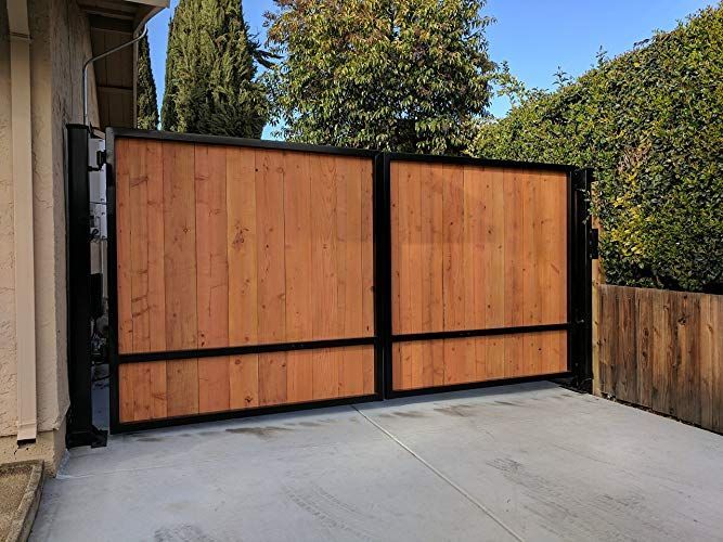 a large wooden gate in the middle of a driveway with trees and bushes behind it