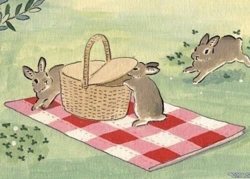 three rabbits are sitting on a picnic blanket with a basket in the foreground, and another rabbit is running towards it