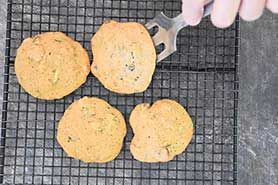 four cookies on a cooling rack with a person cutting them