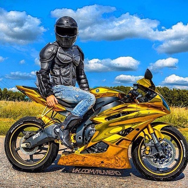 a man sitting on top of a yellow motorcycle in front of a blue sky with clouds